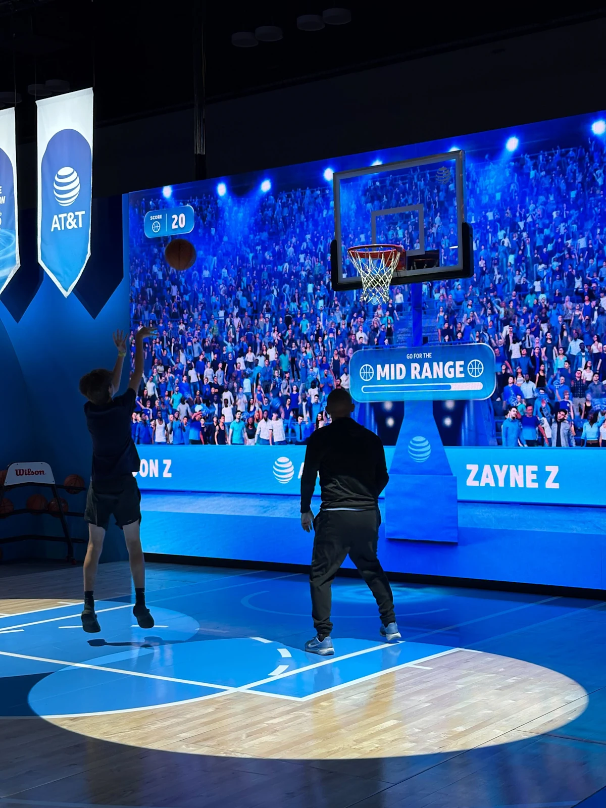 A player shoots toward the hoop in front of the AT&T Live Arena LED wall, displaying live scores and game prompts.